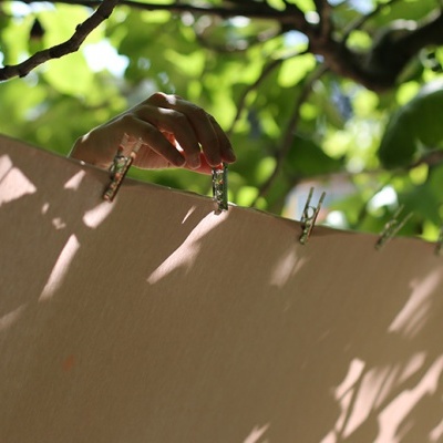Pregadores de madeira seguram tecido bege num estendal com folhas verdes ao fundo