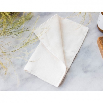 Guardanapo branco dobrado sobre superfície de mármore com plantas secas