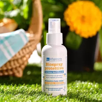 Spray corporal protetor em frasco branco com rótulo colocado sobre relva artificial.