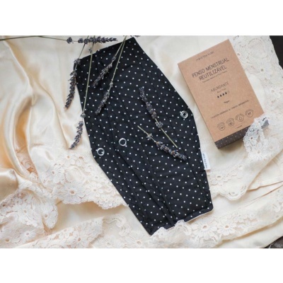 Máscara facial preta com pontos brancos e embalagem de papel castanho sobre tecido bege com renda