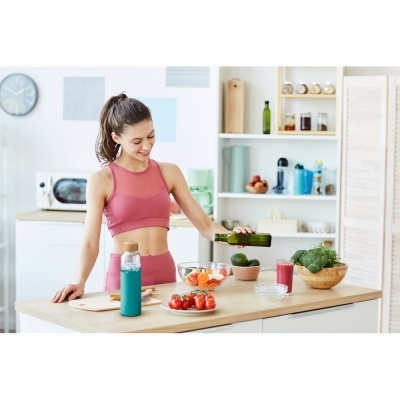 Mulher na cozinha com roupa de exercício cor-de-rosa a preparar bebidas e alimentos frescos na bancada