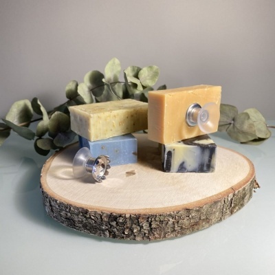 Três barras de sabão coloridas sobre placa de madeira com folhas secas ao fundo