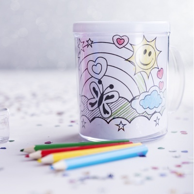 Caneca branca com design para colorir, desenhos de sol, nuvens, corações, estrelas e borboleta, com lápis de cor ao lado.