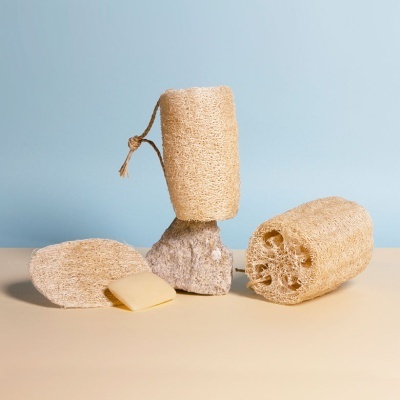 Três esfregões de lufa naturais colocados em superfície amarela clara com fundo azul.