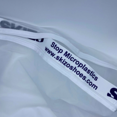 Correia branca com texto azul 'Stop Microplastics www.skizoshoes.com' sobre fundo branco translúcido