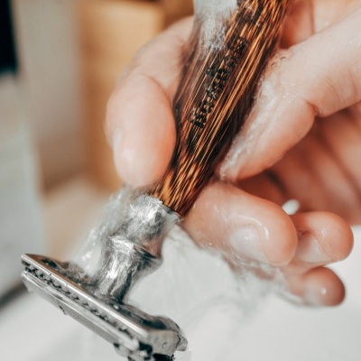 Navalha de barbear com cabo de madeira e metal sendo lavada sob água corrente