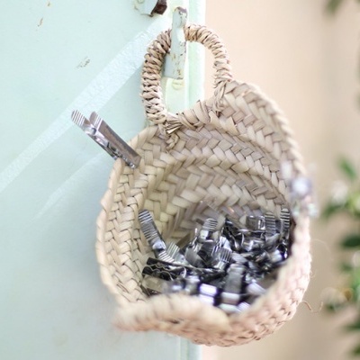 Cesta de palha com cubos de metal pendurada numa parede de vidro junto a planta.