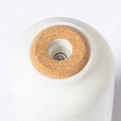 Objeto cilíndrico branco com base em cortiça e componente metálico no centro