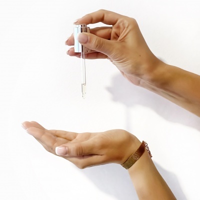 Mãos femininas com conta-gotas transparente e fundo branco.