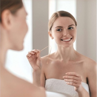 Mulher loira segurando fio dental metálico diante do espelho