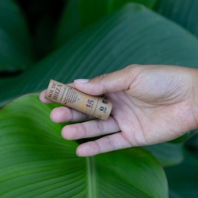 Mão segurando protetor solar em embalagem castanha claro sobre folhas verdes