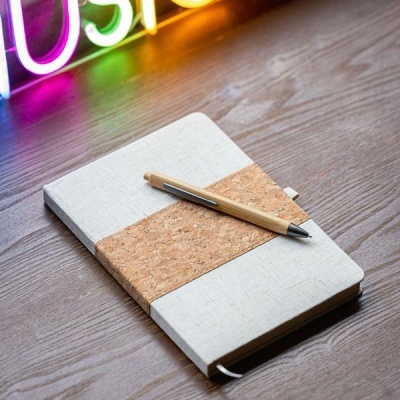 Caderno branco com faixa de cortiça e caneta de madeira sobre mesa de madeira escura