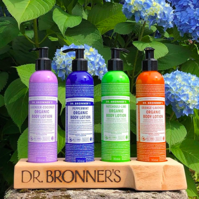 Frascos coloridos de loção corporal Dr. Bronner's organizados em base de madeira com flores de hortênsia ao fundo