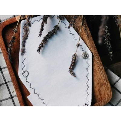 Toalha de papel branca com borda preta recortada em zigzag e tabuleiro de madeira com pano xadrez e ramos de lavanda