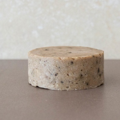 Sabonete redondo bege com grãos escuros sobre superfície castanha