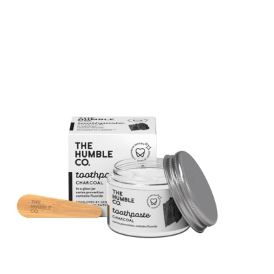 Pasta de dentes preta em frasco de vidro com espátula de madeira e caixa branca da marca The Humble Co.