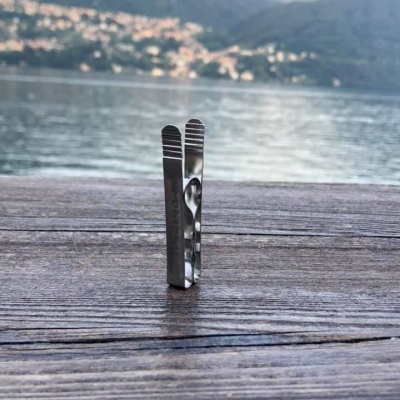 Pinça de metal prateado sobre mesa de madeira junto a rio e montanhas ao fundo