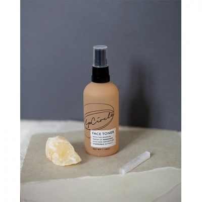 Frasco de tonificante facial UpCircle em fundo cinza com pedra amarela e bastão branco.