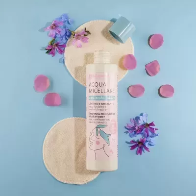 Frasco de Acqua Micellare com flores e discos de algodão em fundo azul