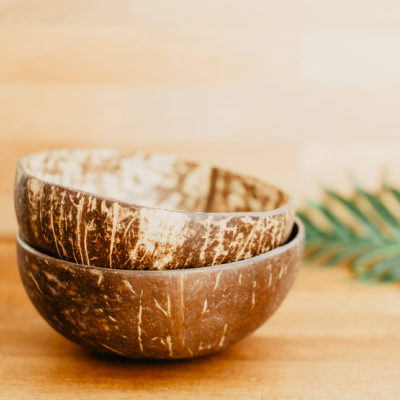 Duas tigelas de casca de coco em superfície de madeira com folha verde ao fundo