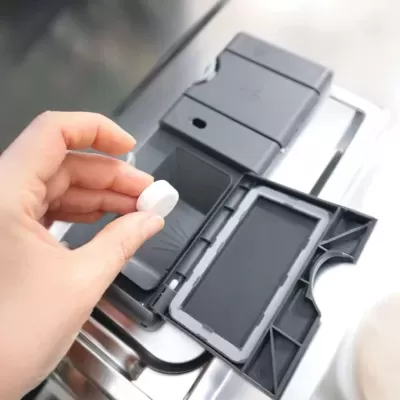 Comprimido branco a ser colocado em dispenser cinzento de máquina de lavar