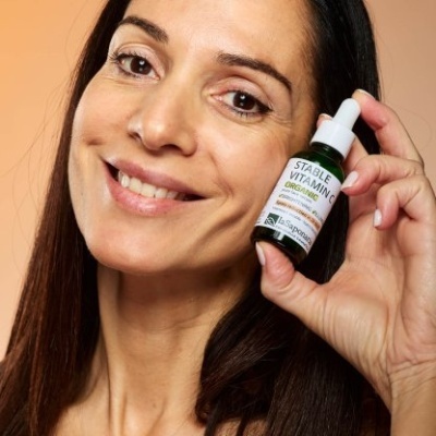 Mulher segura frasco de vitamina C orgânica com conta-gotas em fundo laranja