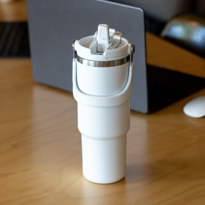 Garrafa térmica branca com tampa e pega numa mesa de madeira