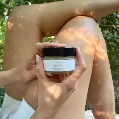 Frasco de creme corporal SOFTNESS segurado sobre pernas nuas ao ar livre