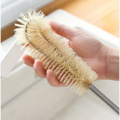 Escova de limpeza com cerdas naturais claras e cabo metálico nas mãos