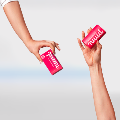 Duas mãos segurando embalagens rosa com o texto muud em fundo claro