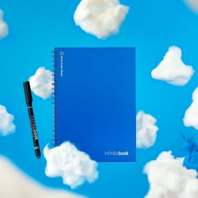 Caderno azul com espiral e caneta preta sobre fundo azul com nuvens artificiais