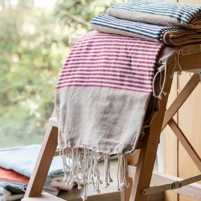 Toalhas riscas vermelhas, azuis e cinza com franjas em suporte de madeira junto a uma janela