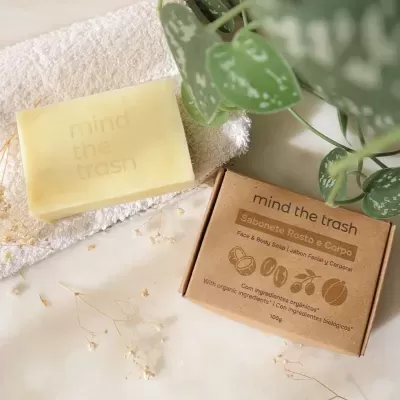 Sabonete amarelo claro com embalagem de papel castanha e plantas verdes ao fundo