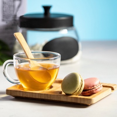 chávena de chá com colher de madeira, macarons sobre tábua de madeira e frasco de vidro ao fundo