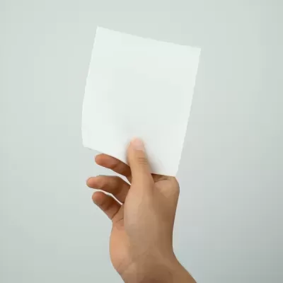 Mão segurando um papel branco quadrado num fundo cinzento claro