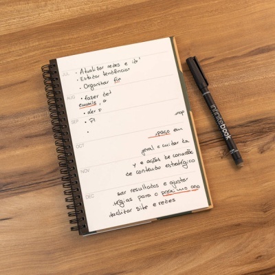 Bloco de notas espiral com anotações manuscritas e caneta preta Infinitebook numa mesa de madeira
