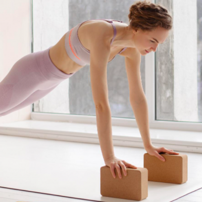 Mulher em posição de prancha usando roupa desportiva cor-de-rosa claro e blocos de yoga castanhos