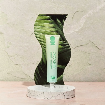 Tubos de creme OdySkin em suporte branco com folhas verdes ao fundo