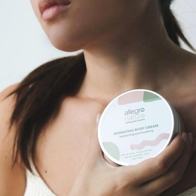 Frasco branco de creme corporal hidratante Allegro Nature segurado por mulher