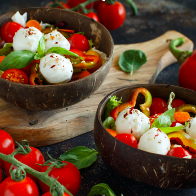 Taças de madeira com salada colorida contendo mussarela, tomates-cereja, manjericão e pimentos.
