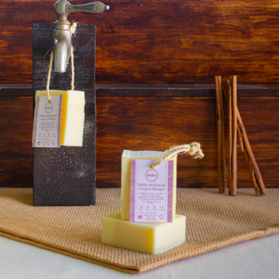 Sabonetes artesanais com etiqueta pendurados e sobre suporte, com paus de canela ao fundo