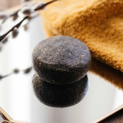 Sabonete sólido preto sobre espelho com toalha amarela ao fundo