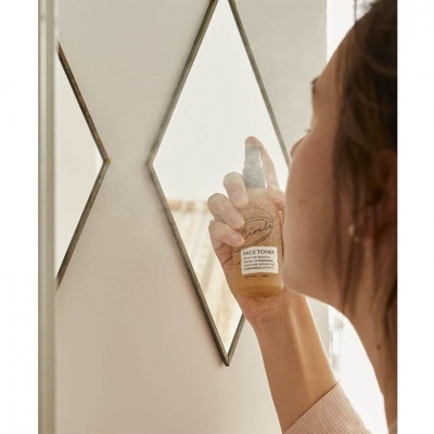 Mulher segura frasco de tónico facial em frente a espelho com moldura em forma de diamante