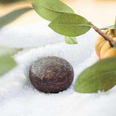 Pedra redonda escura sobre toalha branca com folhas verdes e uma tangerina