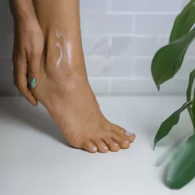 Pé com unhas pintadas e creme aplicado, planta verde ao lado