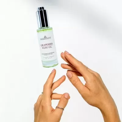 Frasco de óleo puro de toranja com mãos femininas em fundo branco