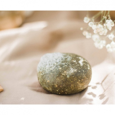 Sabonete sólido cinza com espuma sobre tecido bege e flores brancas