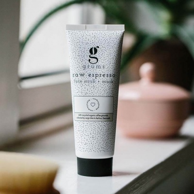 Frasco branco de esfoliante facial Raw Espresso com tampa preta numa superfície branca junto à janela.