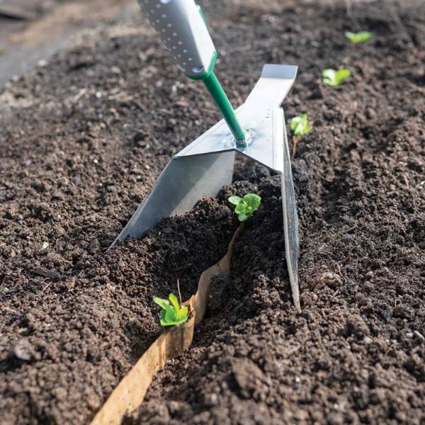 Ferramenta de nivelamento Row Pro sistema Connecta Enxada de metal com cabo verde cavando solo fértil com pequenas plantas verdes
