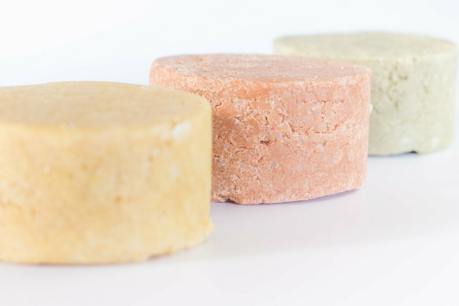 Champô Sólido Cabelos Secos Três barras redondas de shampoo sólido em cores bege, rosa claro e verde claro sobre fundo branco
